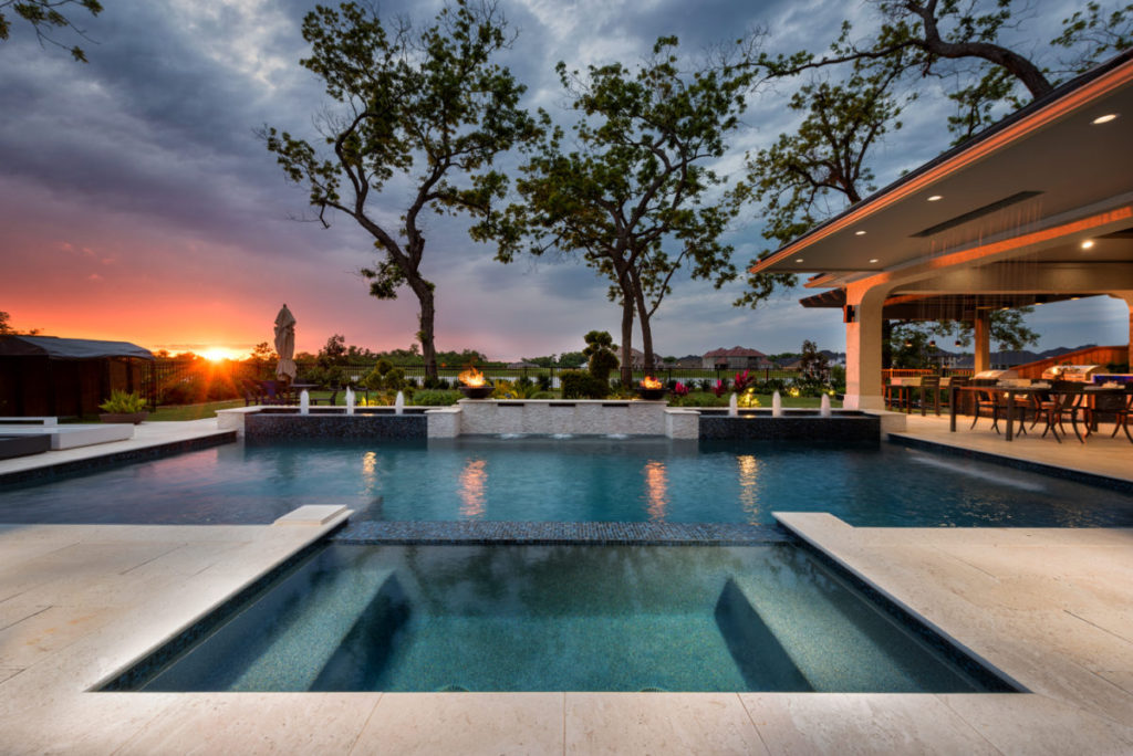 beautiful pool with two trees in the backyard and the sunset off on the left side.
